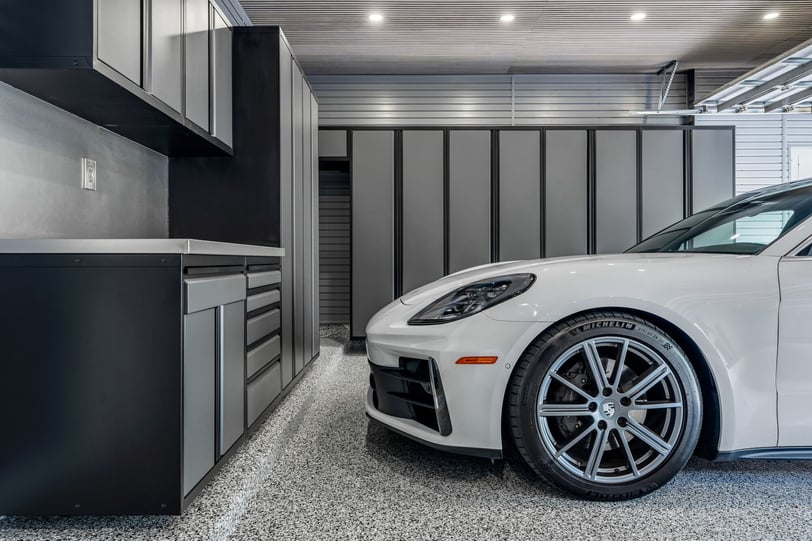 White sports car parked beside floor-to-ceiling grey garage cabinets and lower storage cabinets with a stainless steel worktop.