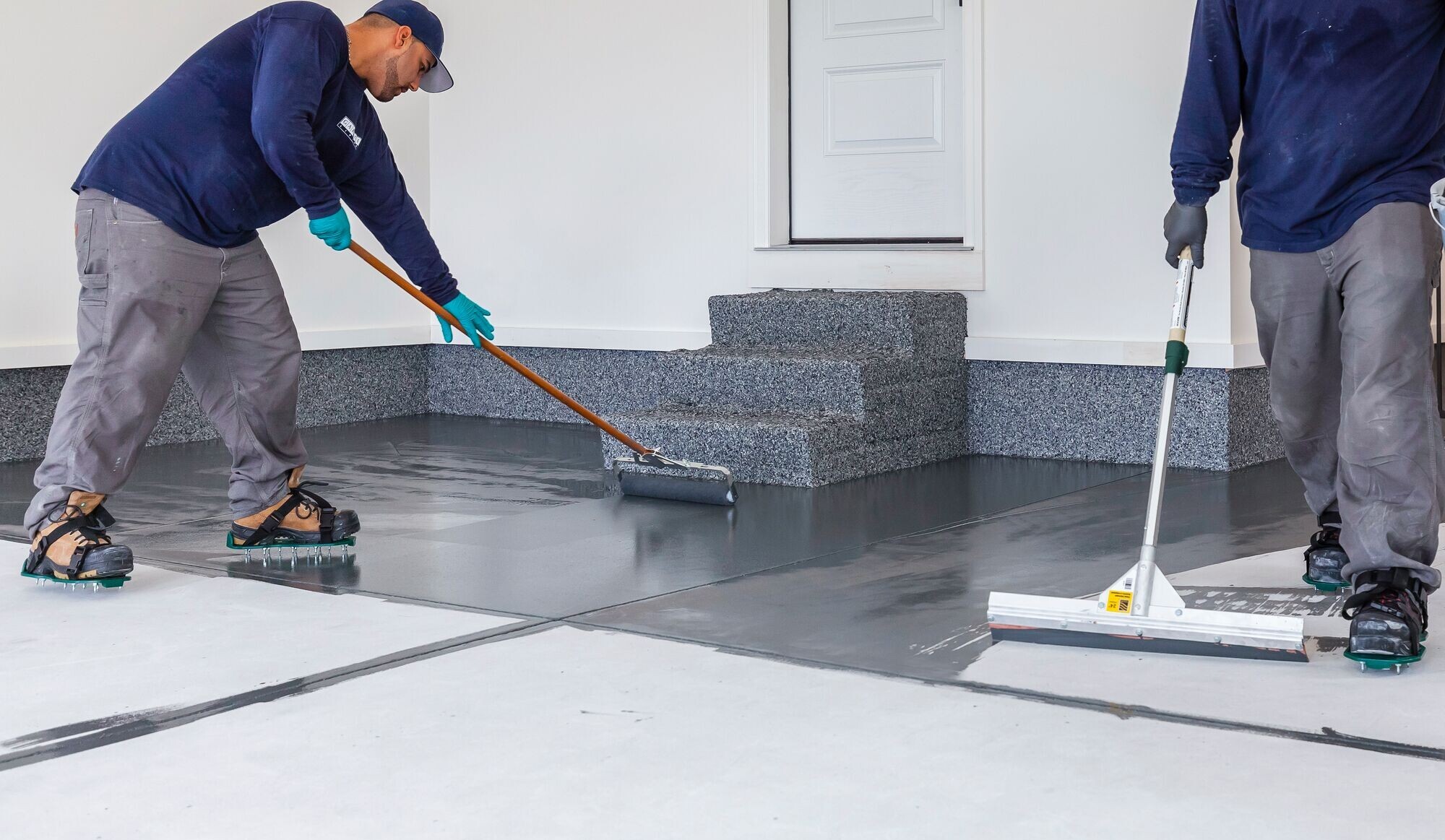 Two professional garage installers are laying down the base for our polyaspartic floor coating