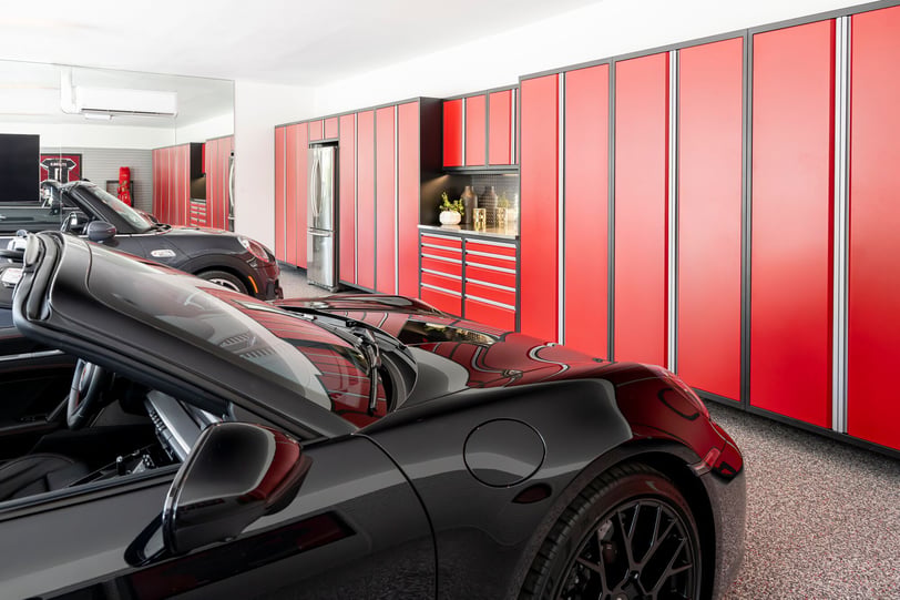 Red floor-to-ceiling garage cabinets with matching drawers and work area beside two black sports cars.