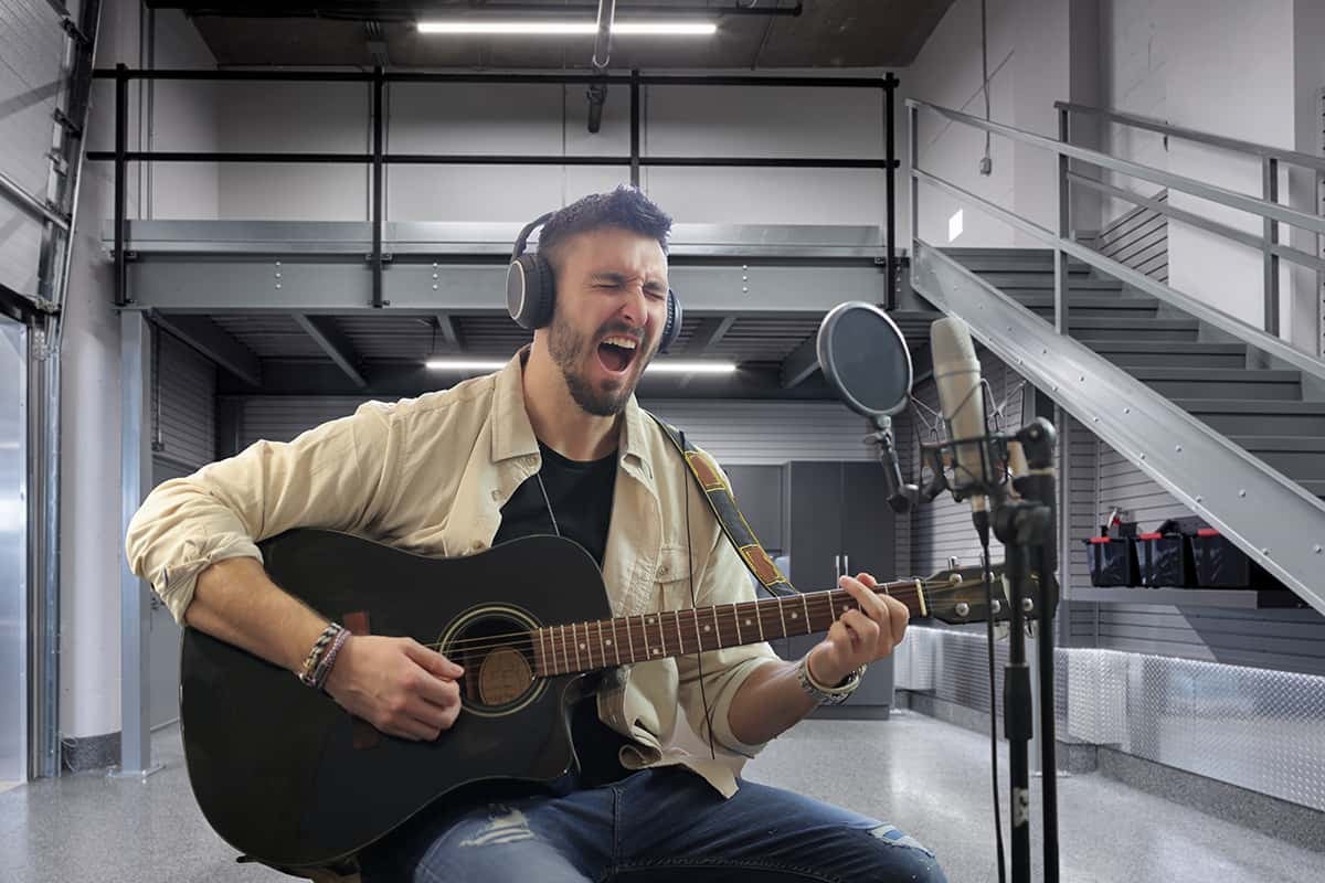 man with guitar singing into microphone in garage