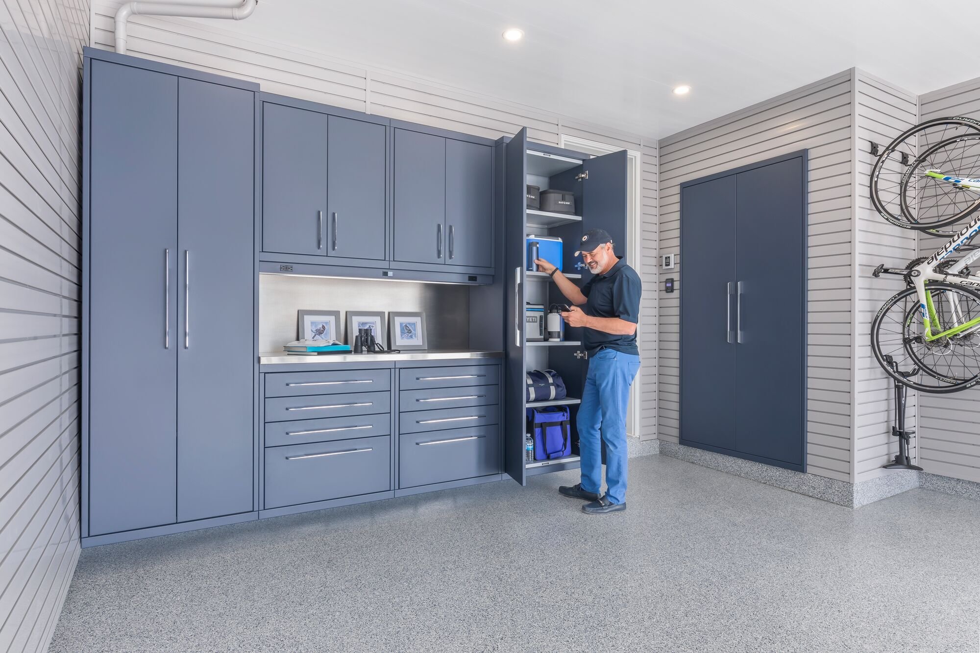 Homeowner opening custom garage cabinets in a fully organized and completed garage renovation