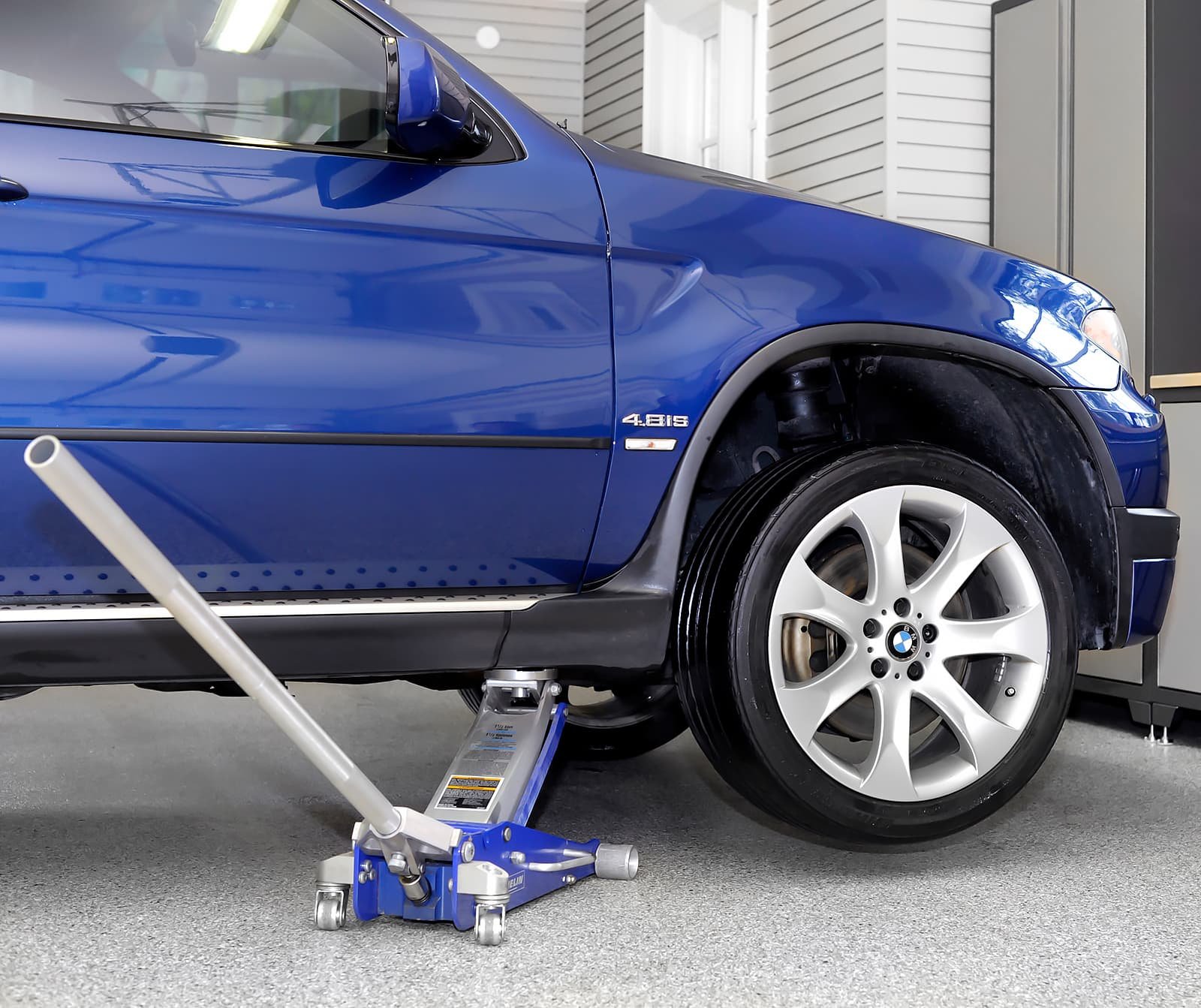 Car jack supporting a blue BMW on a durable polyaspartic floor in garage